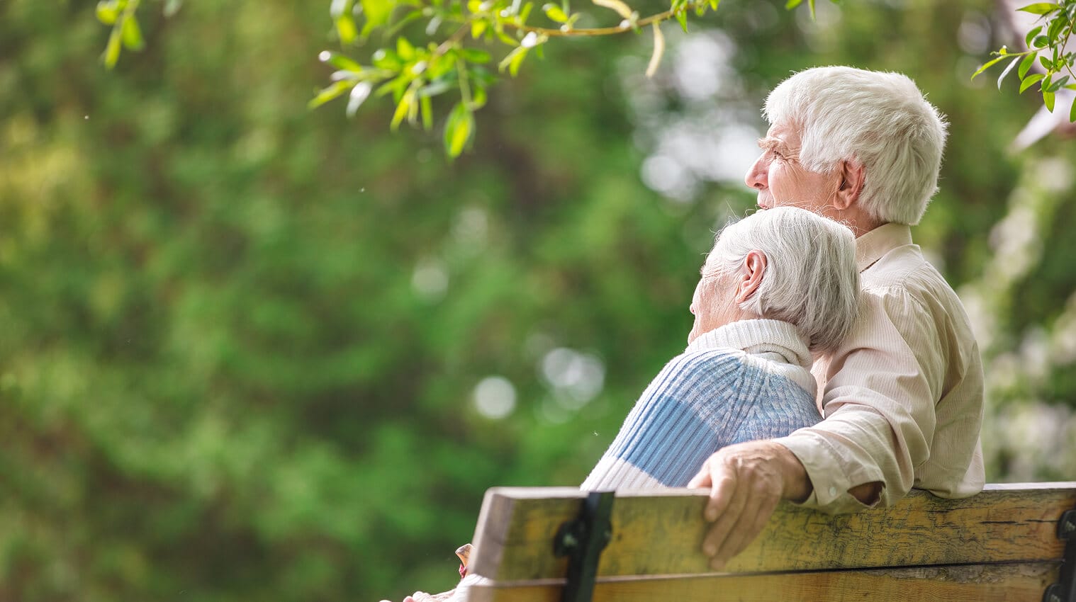 Elderly couple sitting on a park bench, enjoying a peaceful moment together outdoors.