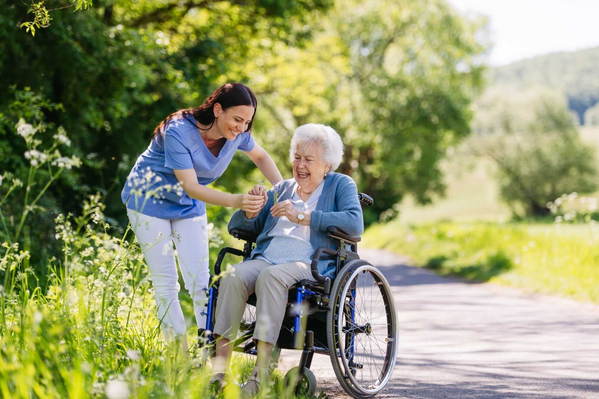 Caregiver helping senior woman in wheelchair pick wildflowers