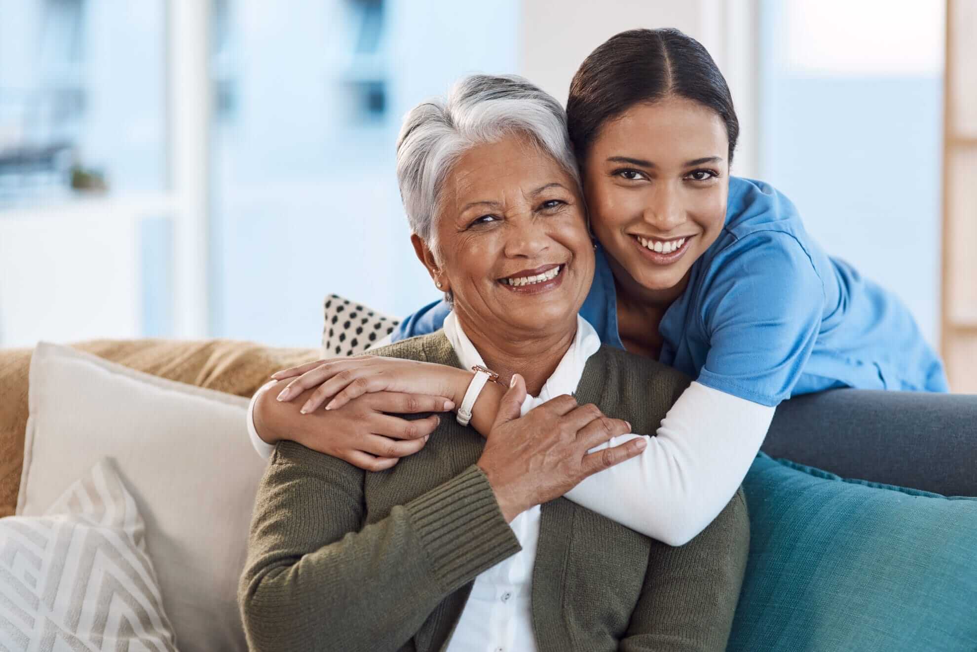 Caregiver embracing elderly woman patient on couch.