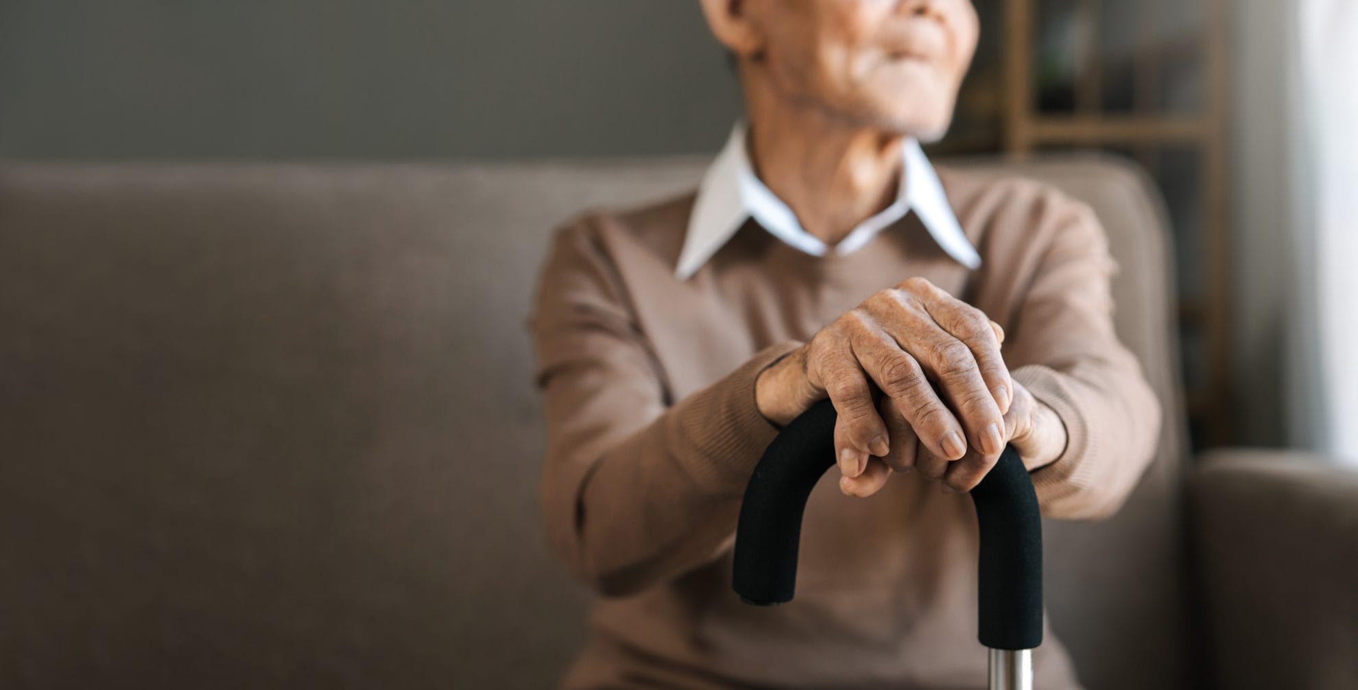 Seated senior man balancing hands on cane and looking out the window.
