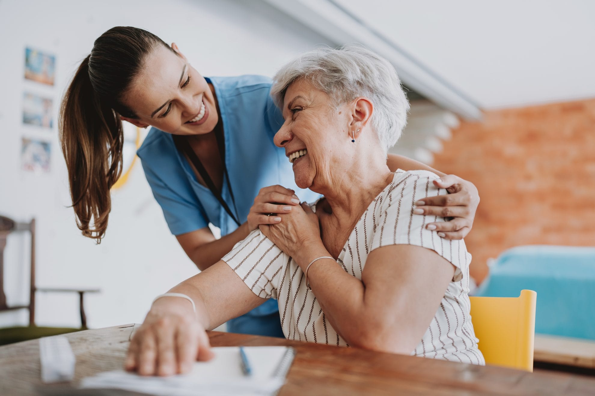 Caregiver embracing woman sitting at table.